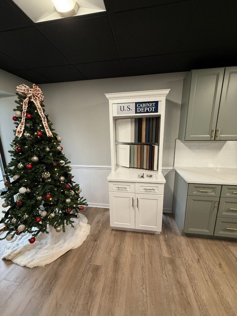 Christmas tree with a large bow, white cabinet with samples, and a cabinet in a room.