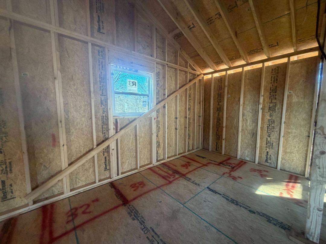 Interior view of a wooden framed room under construction, with a window and angled roof supports.