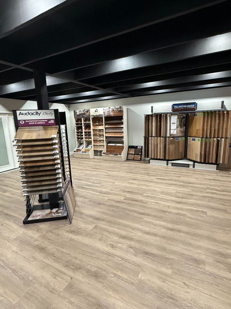 Flooring showroom with wood samples on display. Wooden flooring covers the floor. Black ceiling with lights.
