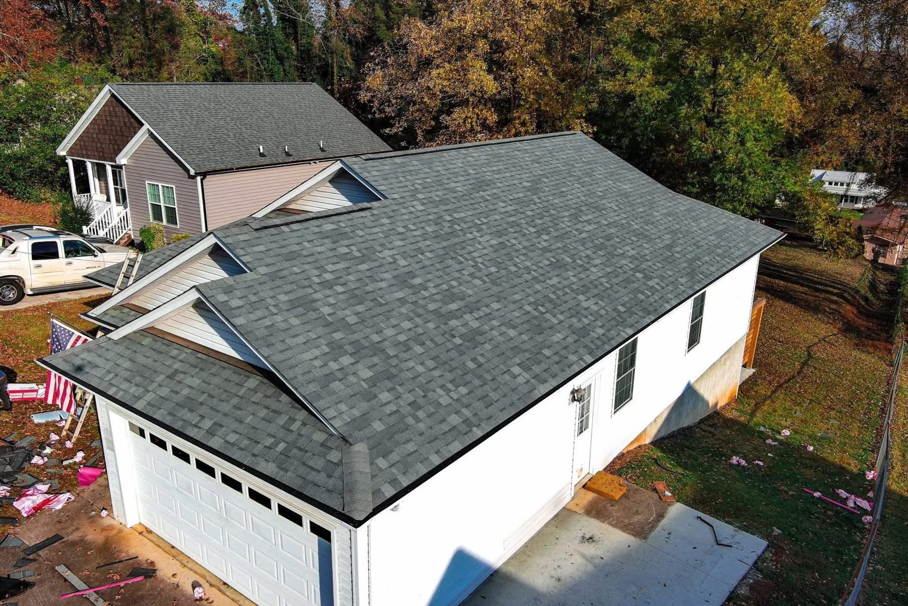 Newly constructed white house with dark gray shingle roof and two-car garage. Another house and trees in the background.