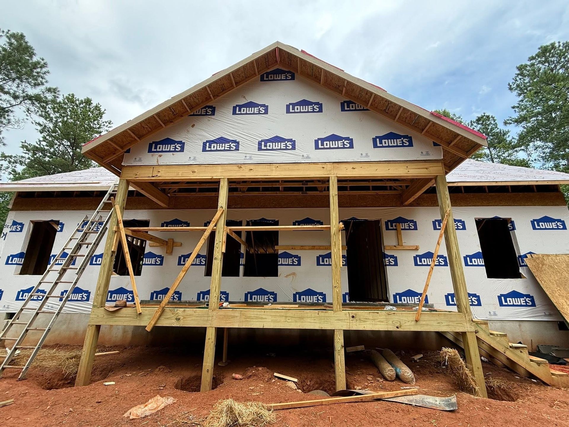 House under construction in a field; unfinished wood structure, blue tarp, golden sunset.