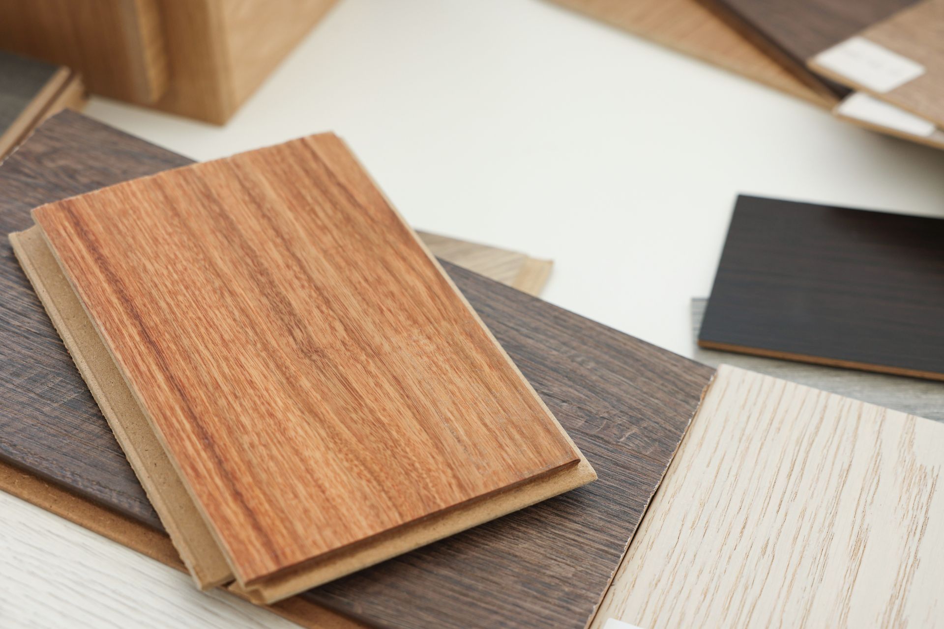 Wooden flooring samples in various colors, stacked on a white surface.