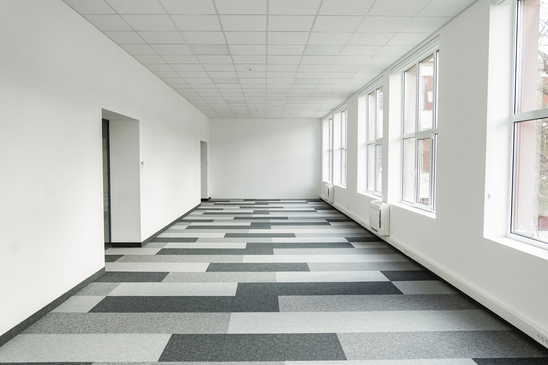 Empty office space with a patterned floor, white walls, and large windows.