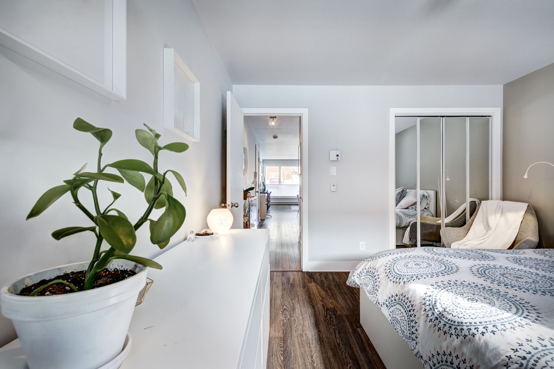 Bedroom interior with plant, white dresser, bed, and open door to hallway.