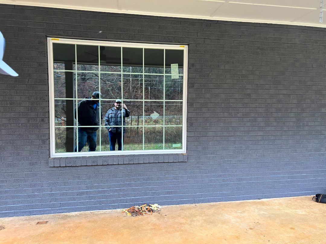 Gray brick exterior with a large window reflecting two people standing outside.