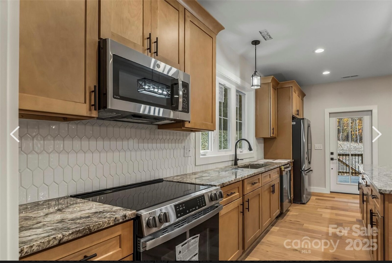 Bright white kitchen with island, cabinets, and appliances on hardwood floor.