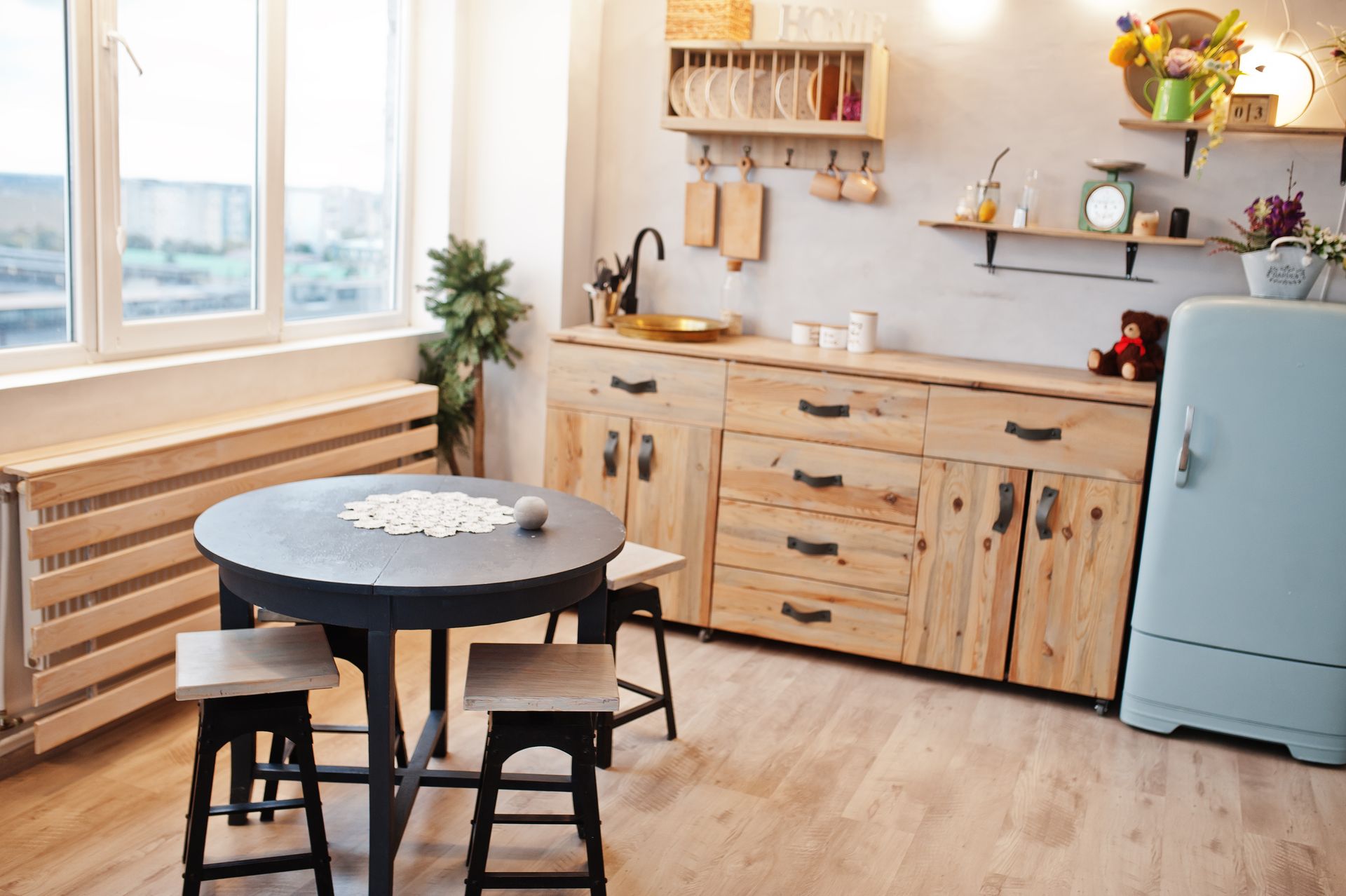 Cozy kitchen with wooden cabinets, round table, and light blue refrigerator. Sunlight streams through the window.