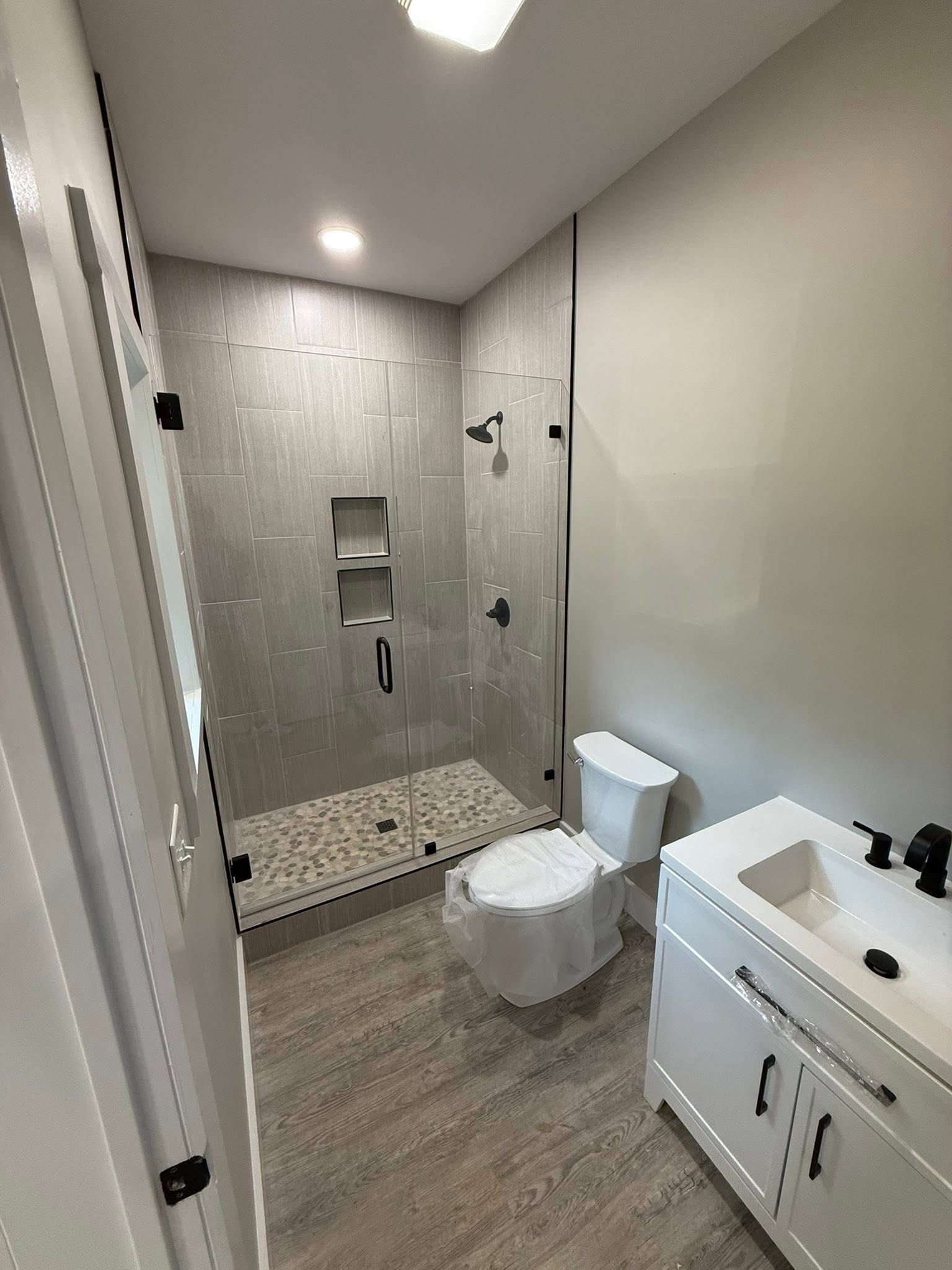 Modern bathroom with a glass-enclosed shower, toilet, white vanity, gray walls and flooring.