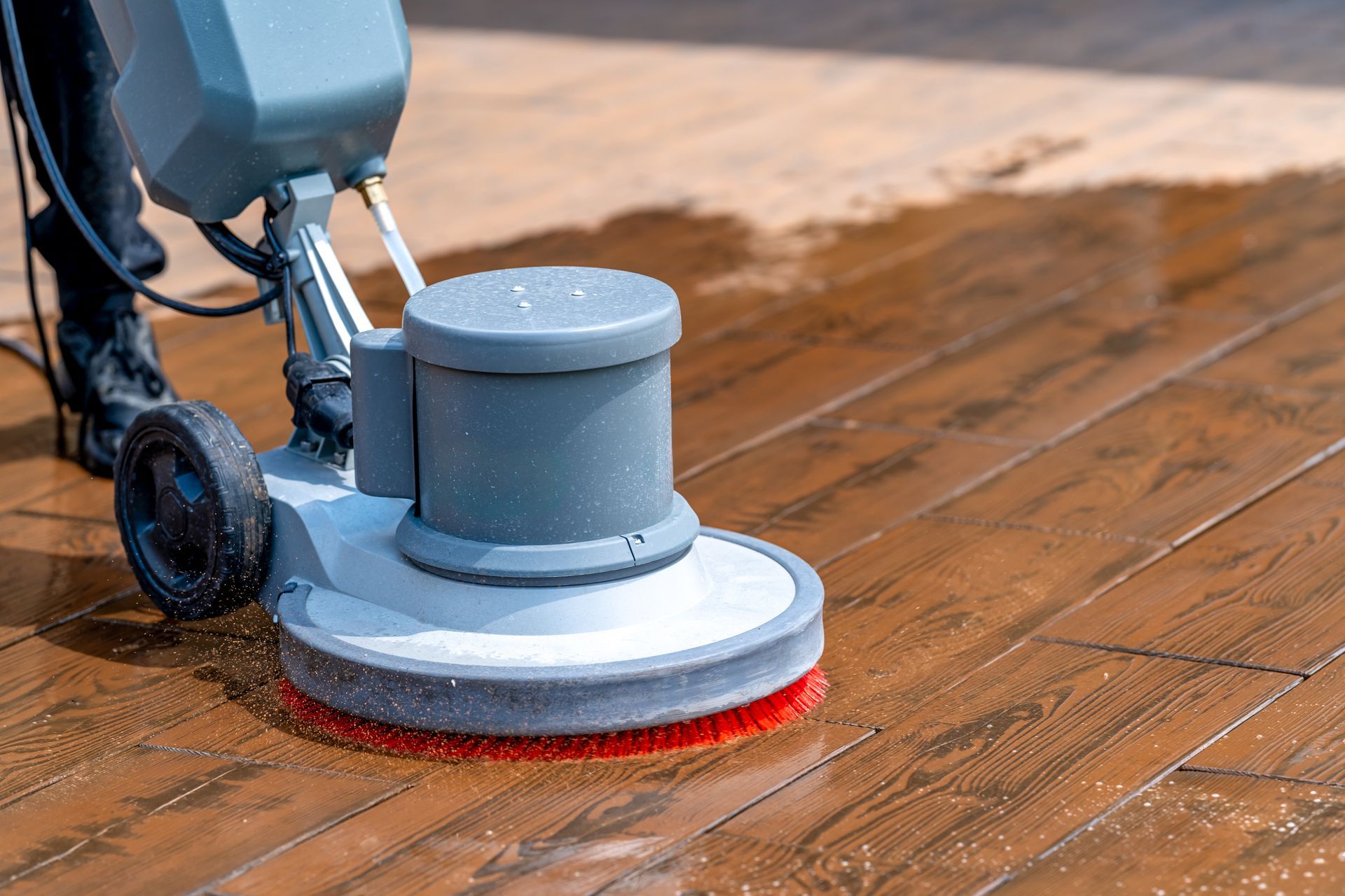 Floor cleaning machine scrubbing wooden planks.