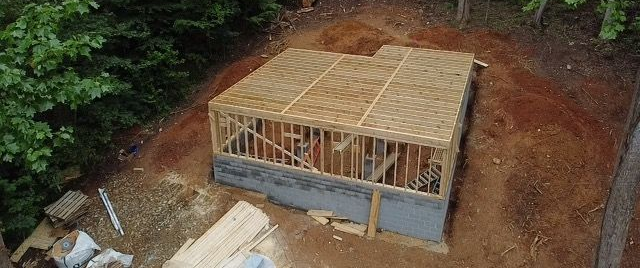 A new construction foundation with initial studs laid is on a cleared propery. 