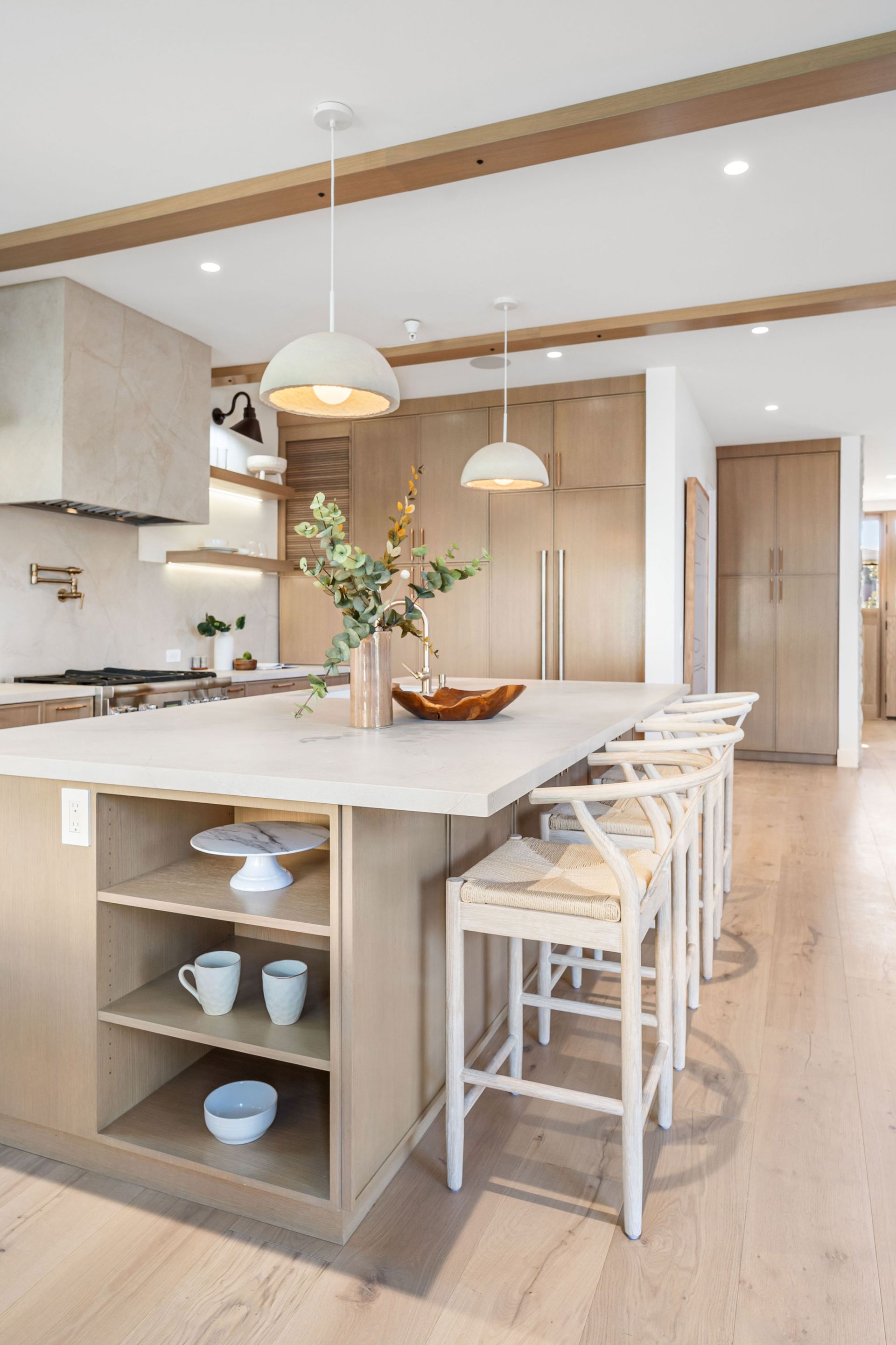 Modern kitchen with light wood cabinets, large island, pendant lights, and bar stools.