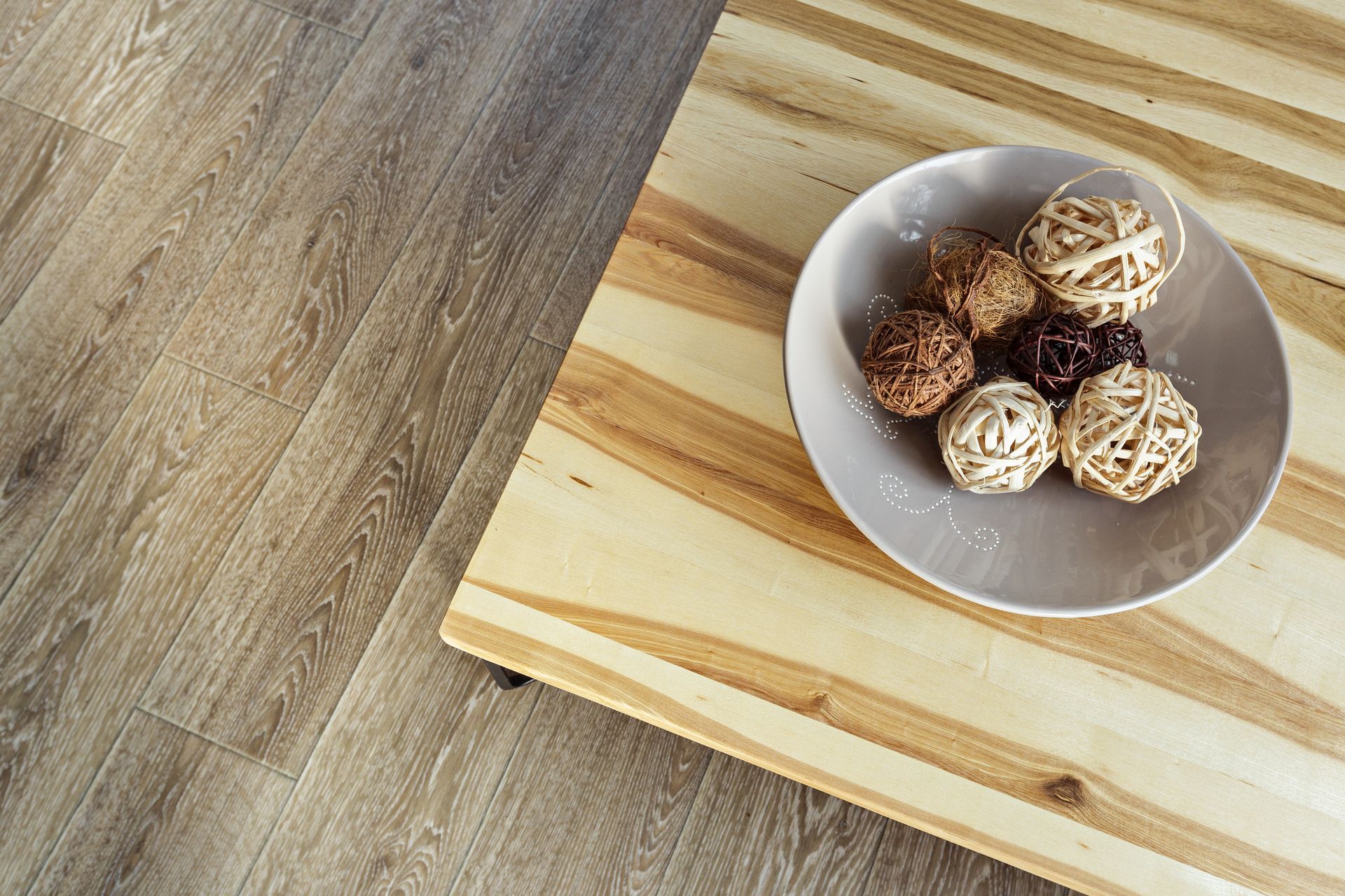Wooden table with a bowl of decorative balls, next to light-brown wood-grain floor.