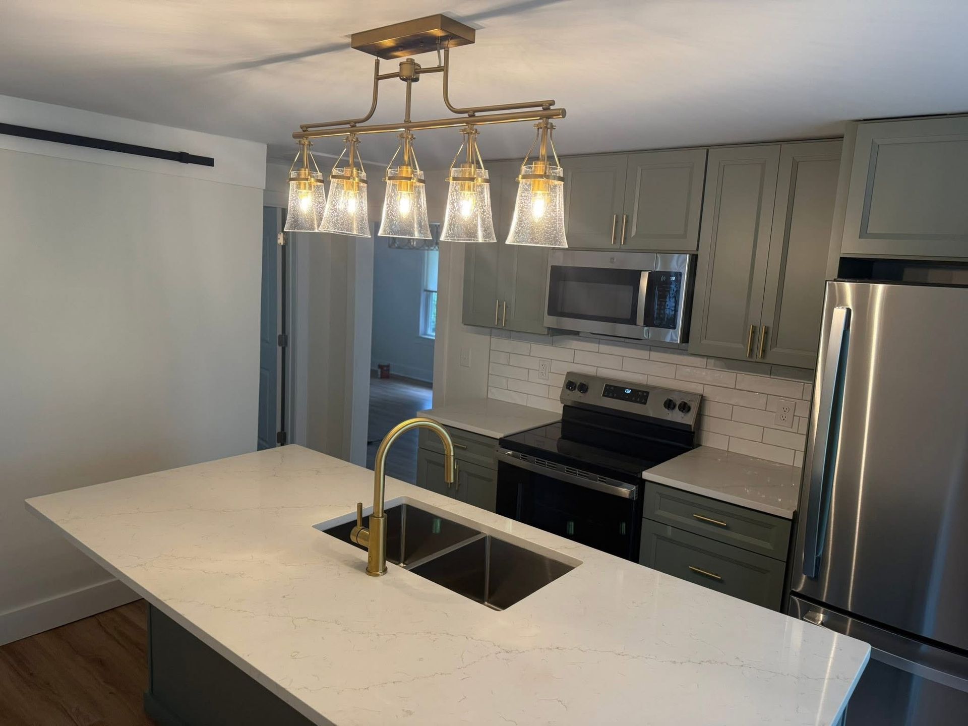Modern kitchen with green cabinets, white countertop island, gold fixtures, and a stainless steel refrigerator.