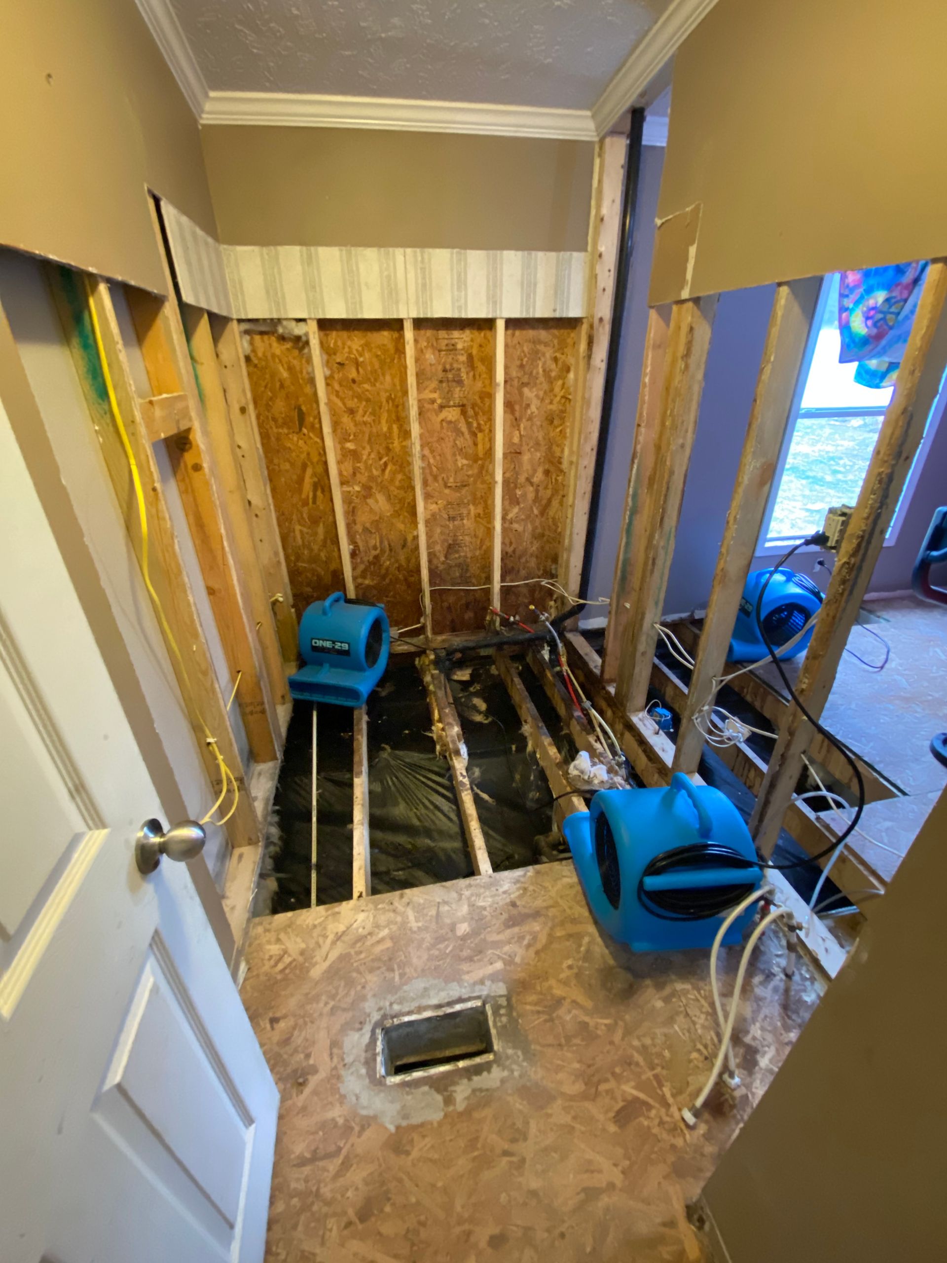 Bathroom under renovation; exposed studs, two blue air movers drying the floor, and unfinished walls.