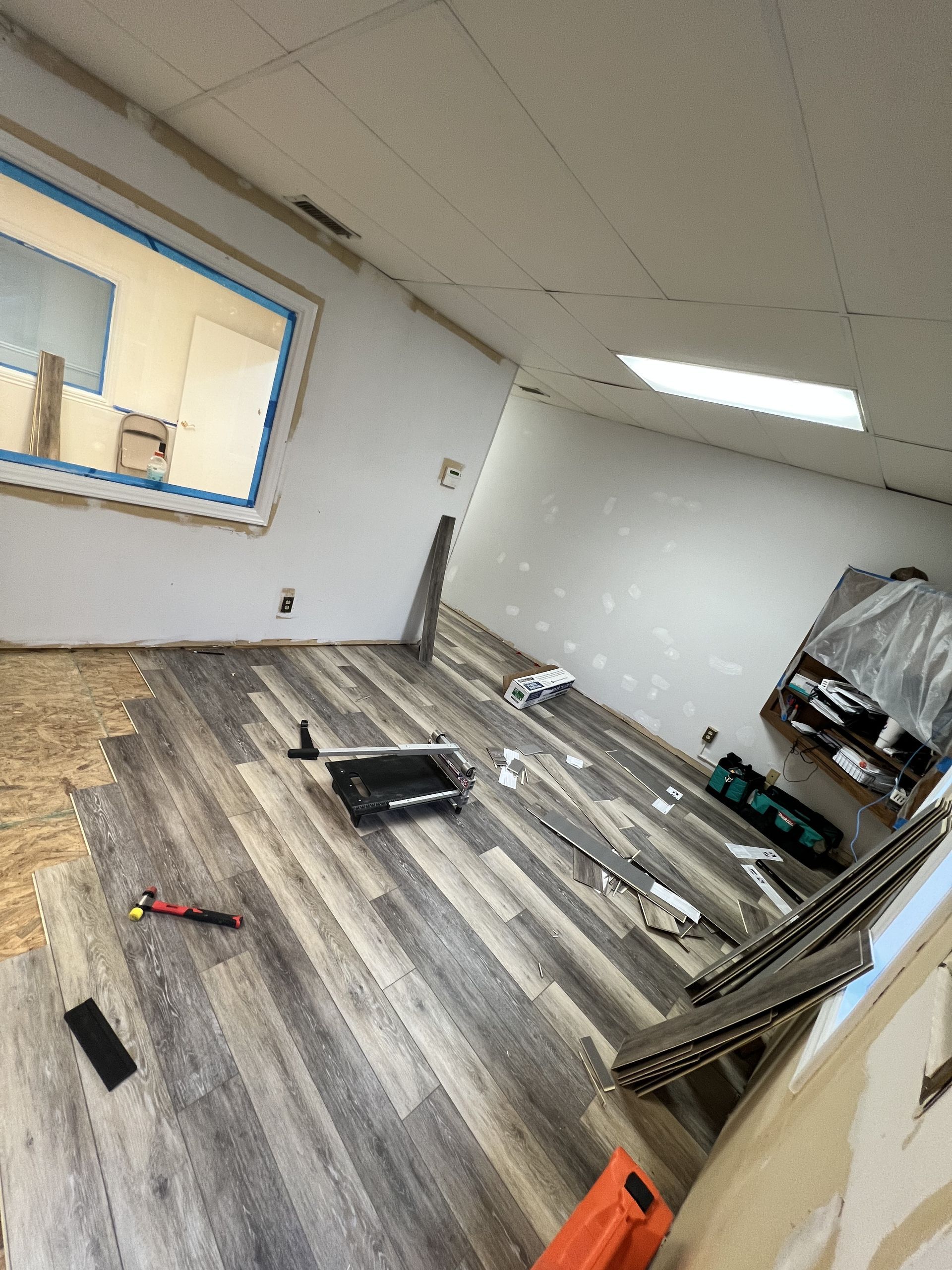 Room under renovation, new wood-look flooring installed. Tools and materials scattered throughout the room.