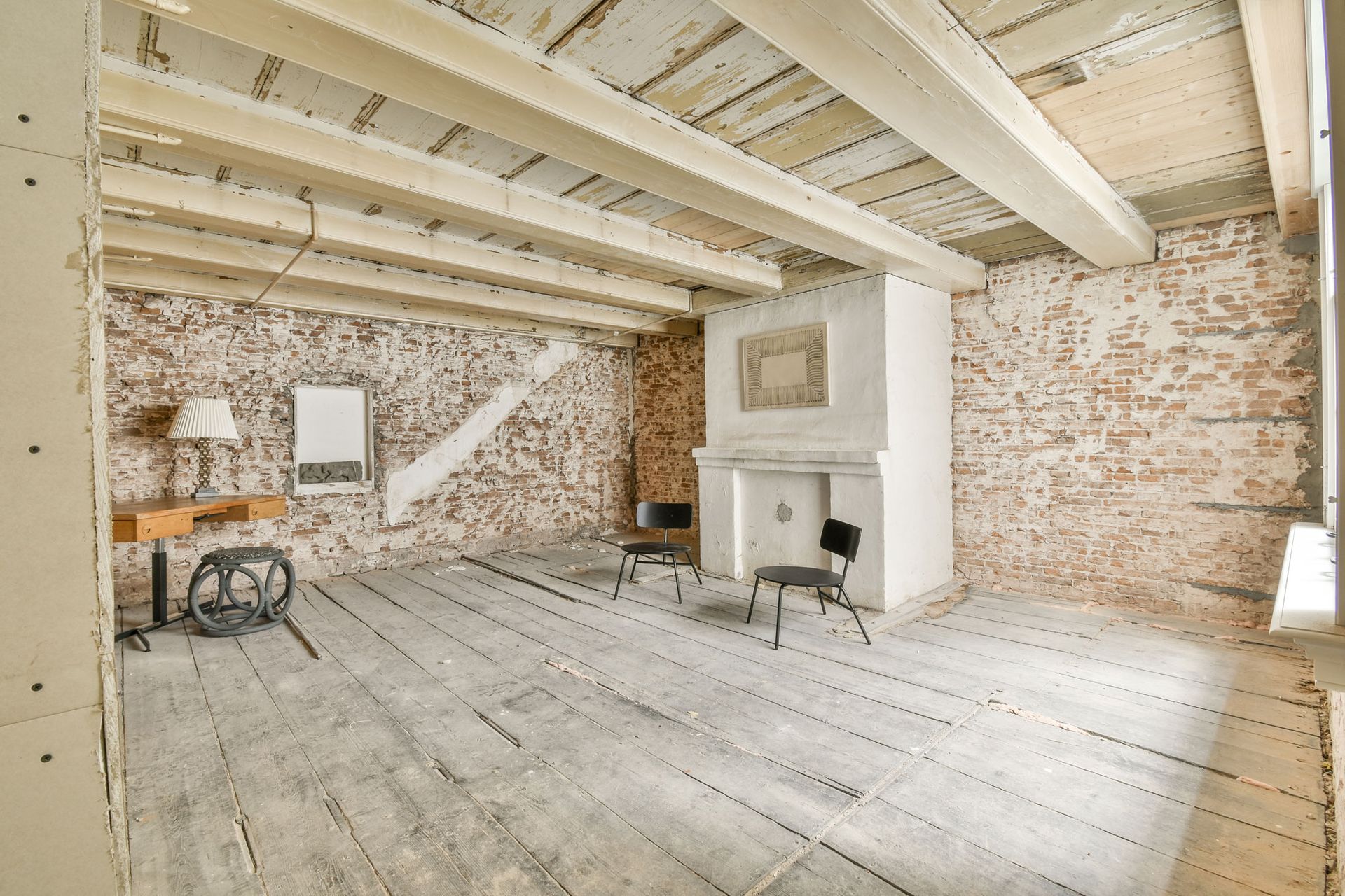 Room interior undergoing renovation, exposed brick walls, wooden beams and floor, fireplace.