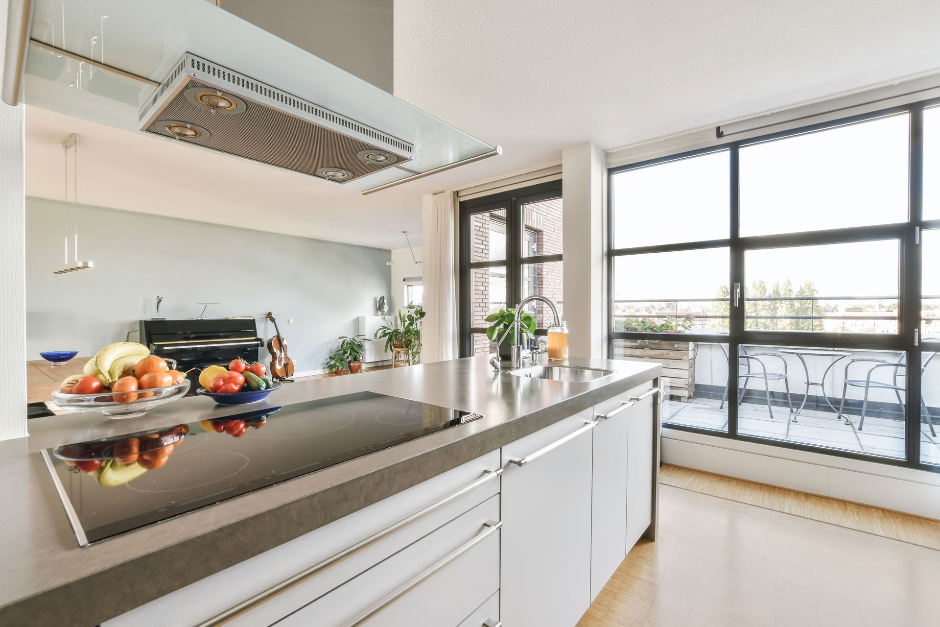 Modern kitchen with island, cooktop, and balcony view. White cabinets, gray countertop, black appliances.