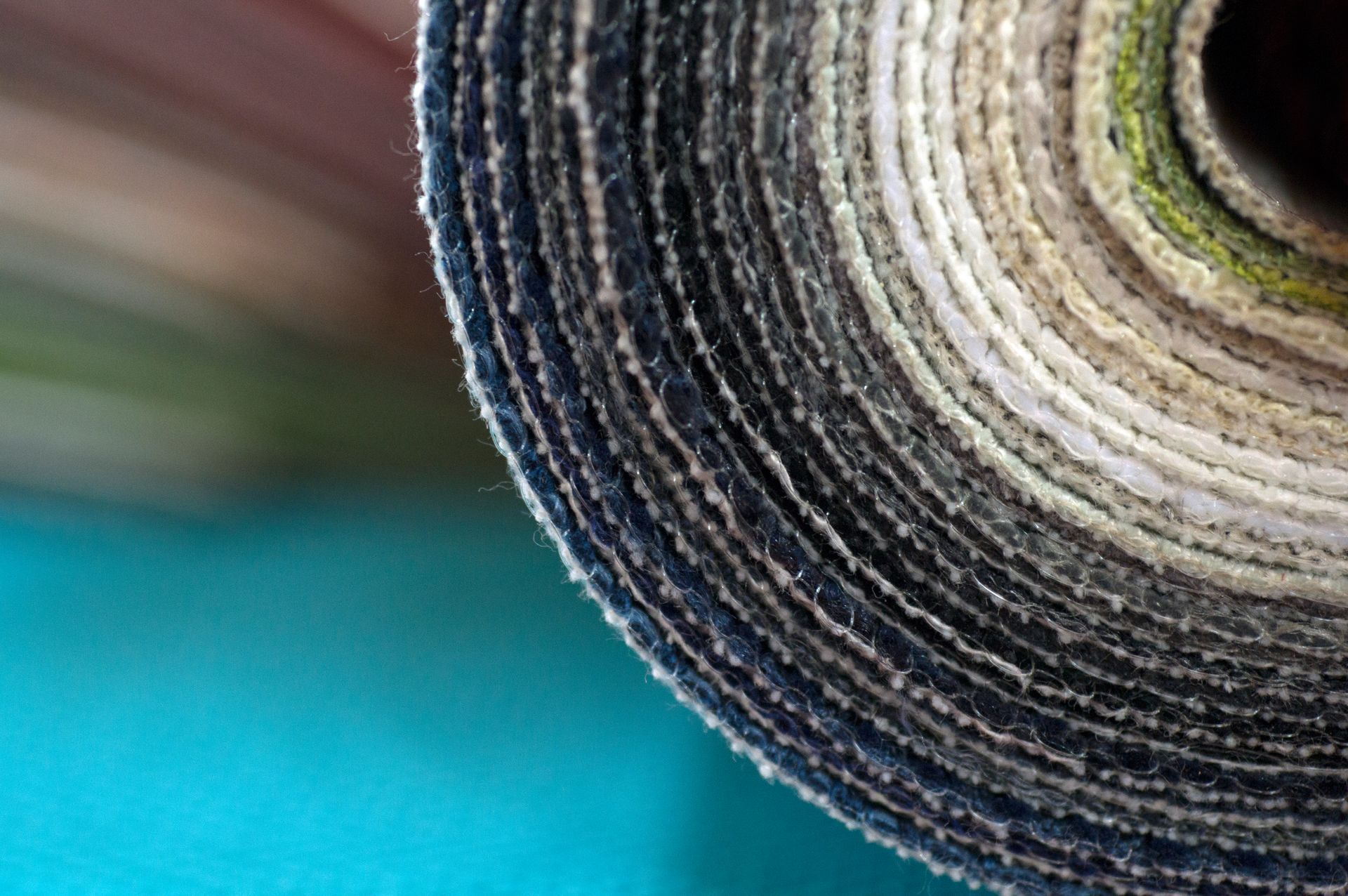 Close-up of a rolled-up fabric, showing layers of different shades of gray, white, and green against a teal background.