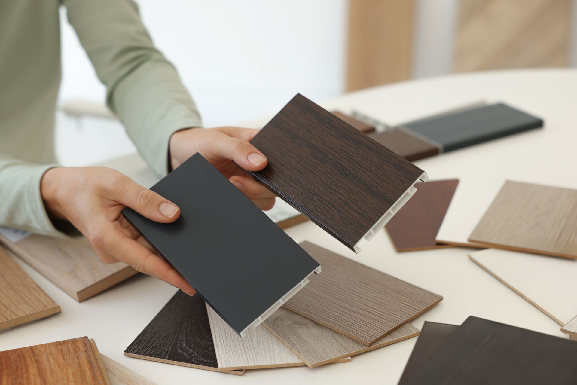 Person holding two dark wood samples, comparing against a table of various flooring colors.