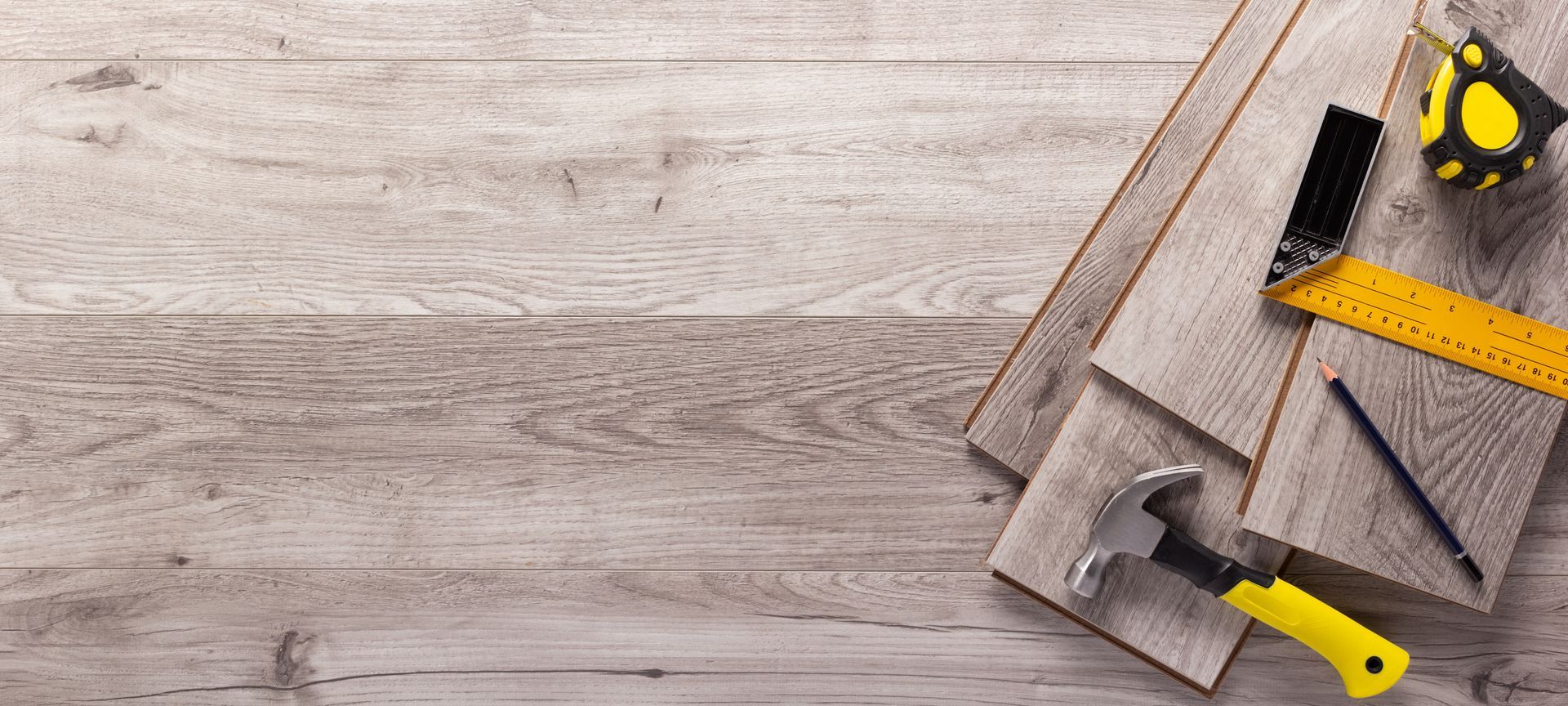 Wooden floor with tools: hammer, ruler, pencil, and tape measure.