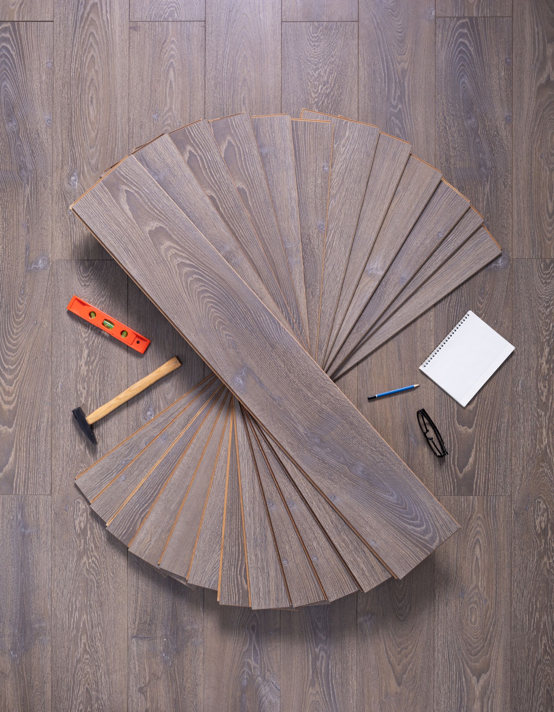 Wooden floorboards arranged in a fan shape with tools on a hardwood floor.