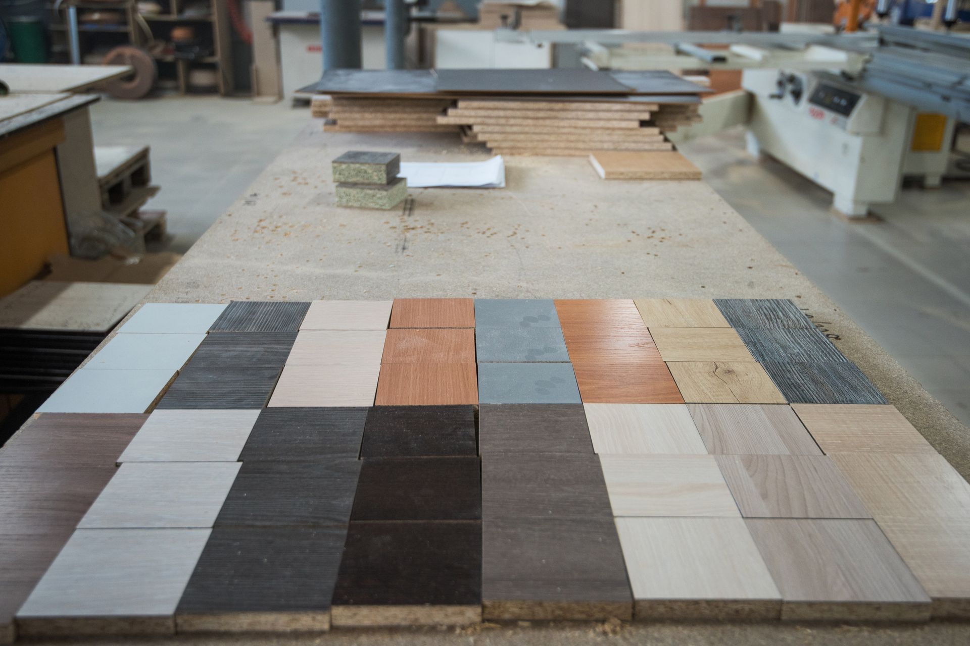 Samples of various wood and laminate materials arranged on a workbench in a workshop setting.