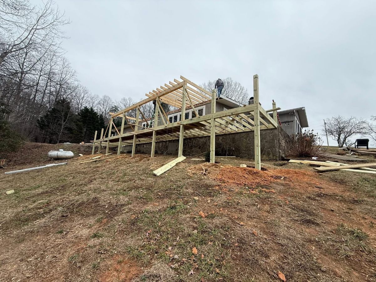 Wooden deck under construction on a hillside, with posts, beams, and a partial roof structure.