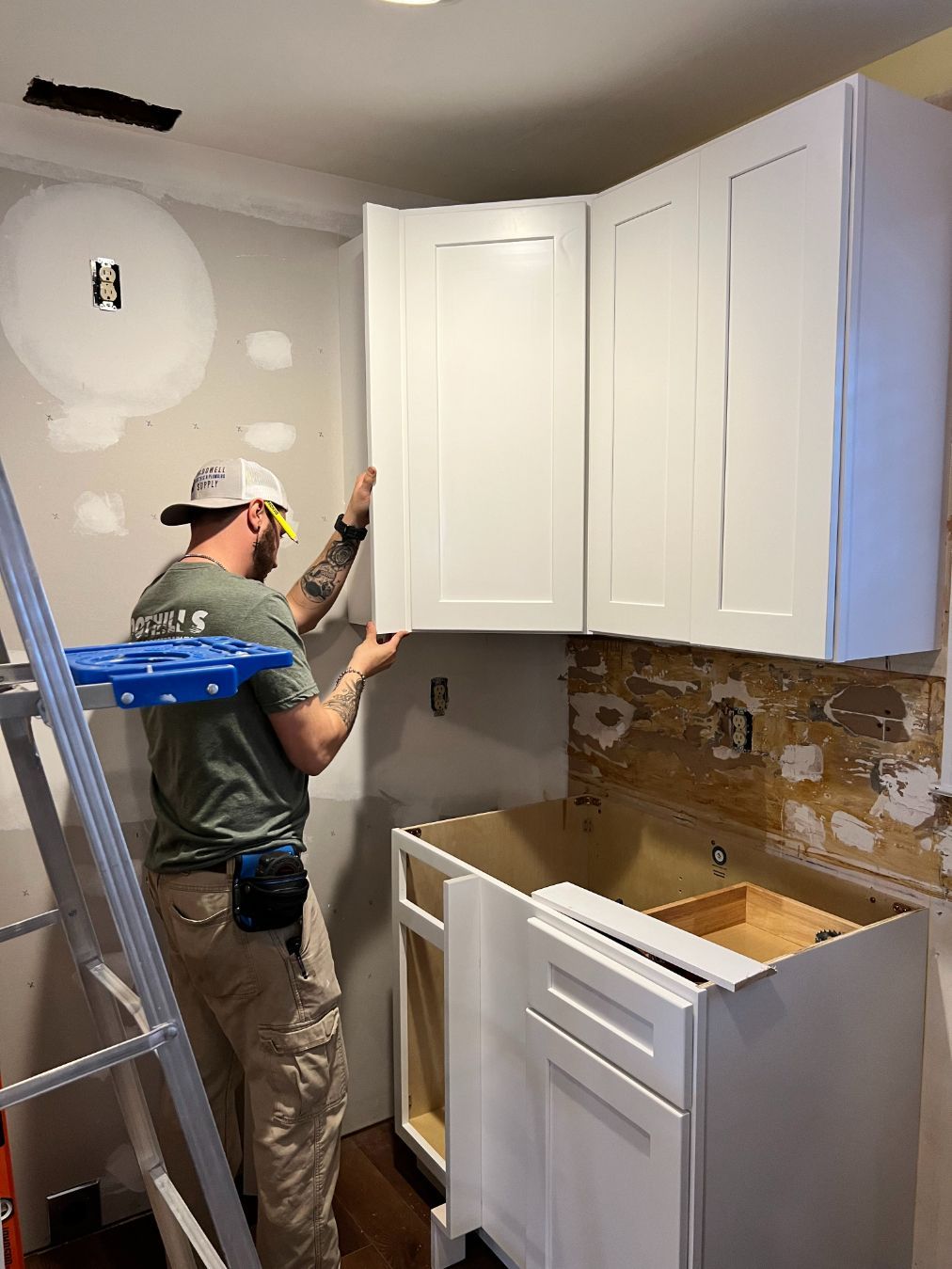 Person installing white kitchen cabinets. Interior setting, ladder present.