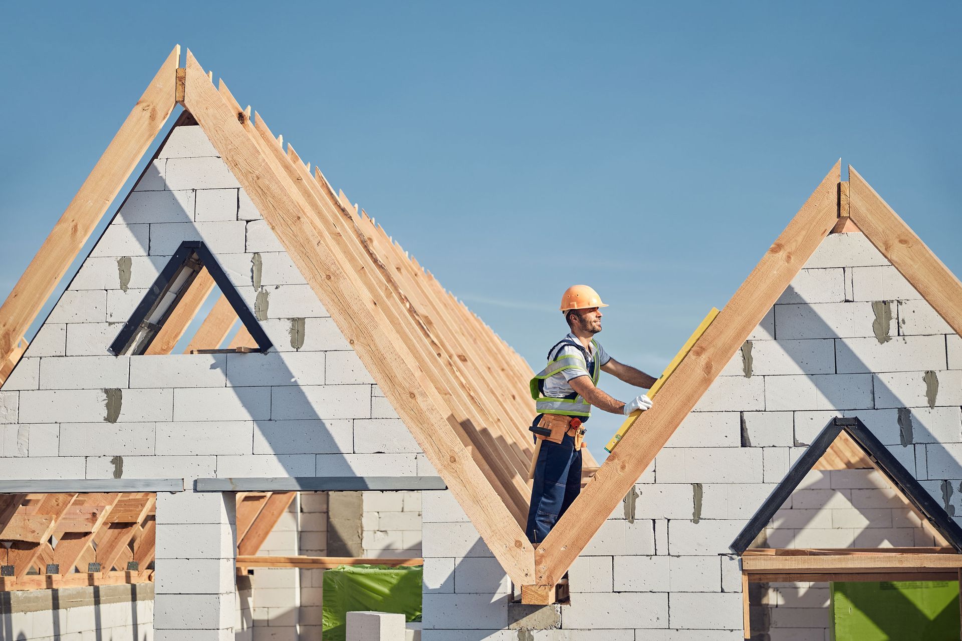 Construction worker on roof frame, measuring wooden beams, blue sky.