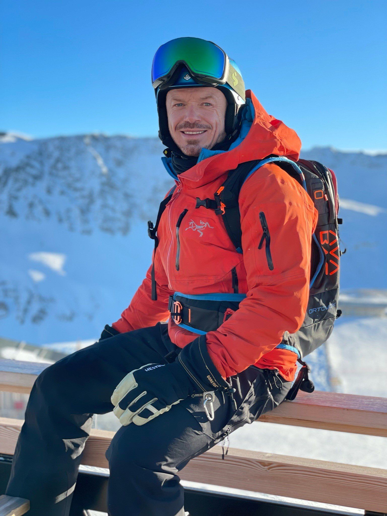 A man in an orange jacket is sitting on a bench in the snow.