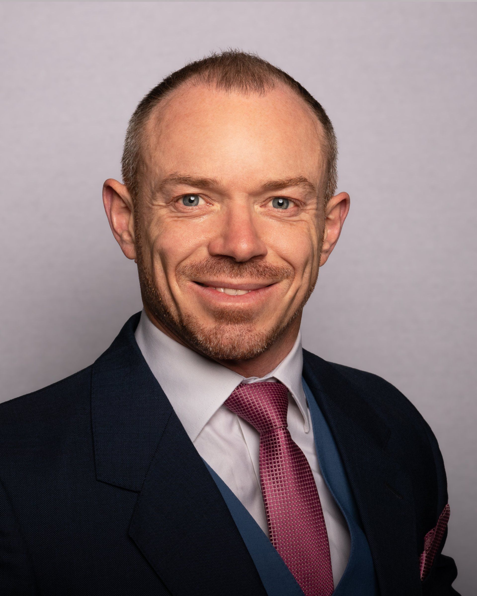 Dr Owen Wall in a suit and tie is smiling for the camera.