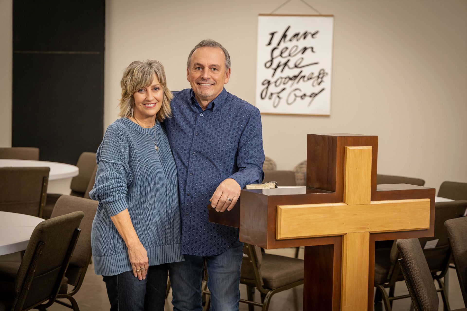 A man and a woman are standing next to a cross in a room.