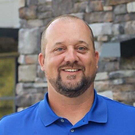A man with a beard is wearing a blue shirt and smiling.