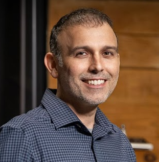 A man in a blue plaid shirt is smiling for the camera.