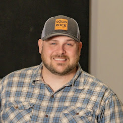 A man wearing a plaid shirt and a hat with the word solid rock on it.