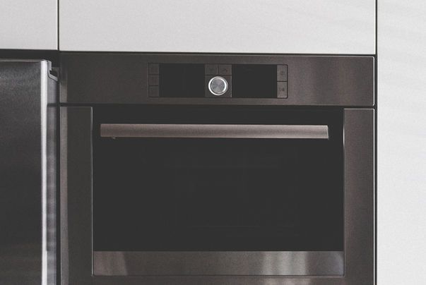 Black built-in oven with a digital display and a stainless steel handle, set in a white kitchen.