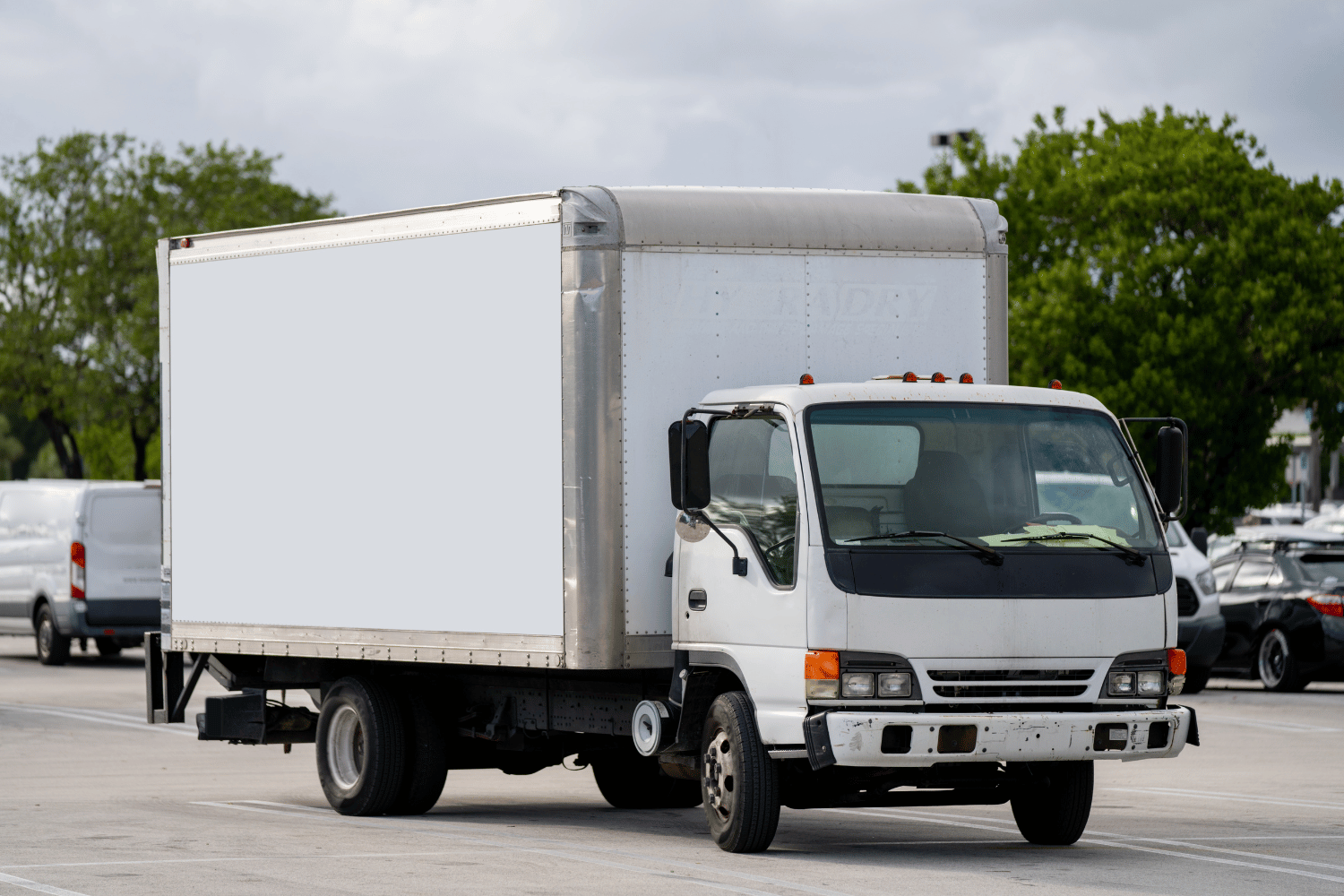 White box truck parked outdoors in a lot, side view with trees in the background