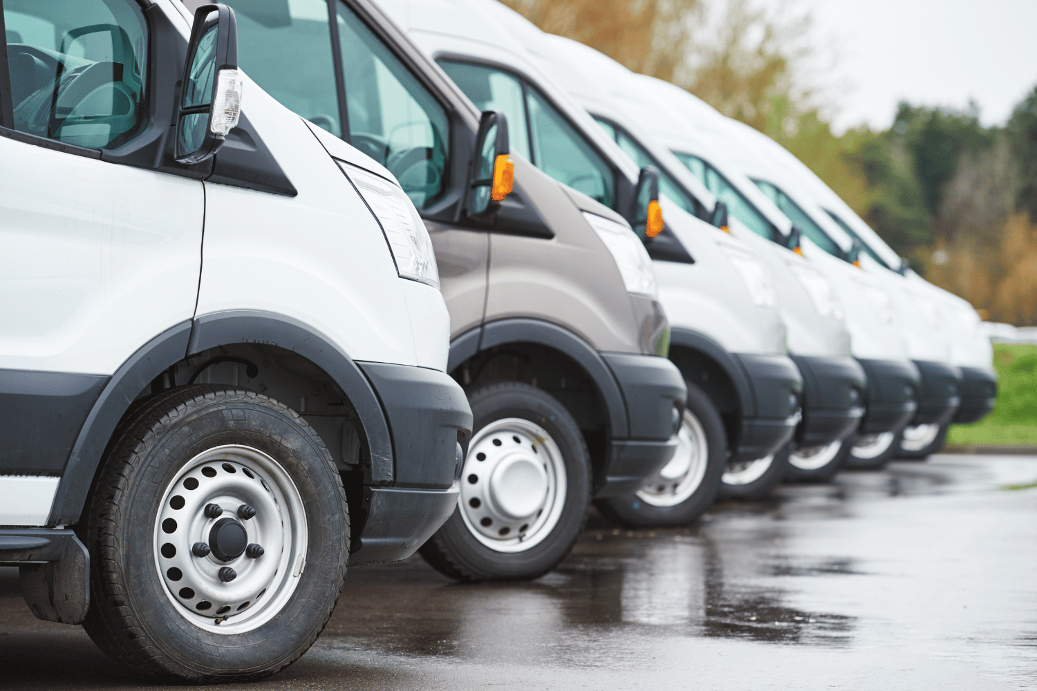 Row of parked white and gray delivery vans on a wet lot
