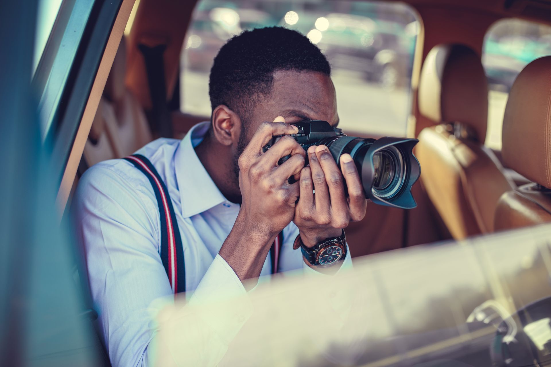 A person aiming a DSLR camera with a telephoto lens from a car window.