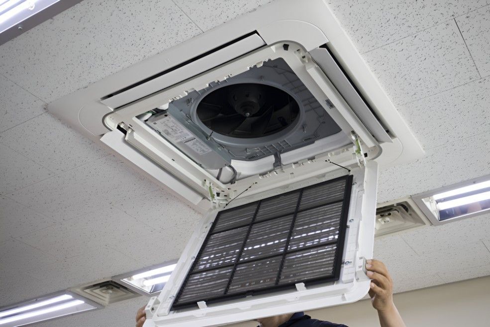 A Man is Holding a Filter in Front of an Air Conditioner — Cooling Plus Refrigeration & Airconditioning in Ciccone, NT