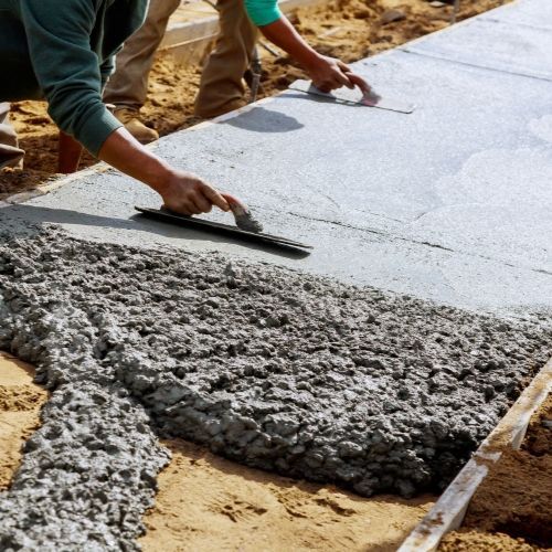 A man is spreading concrete on a sidewalk with a trowel