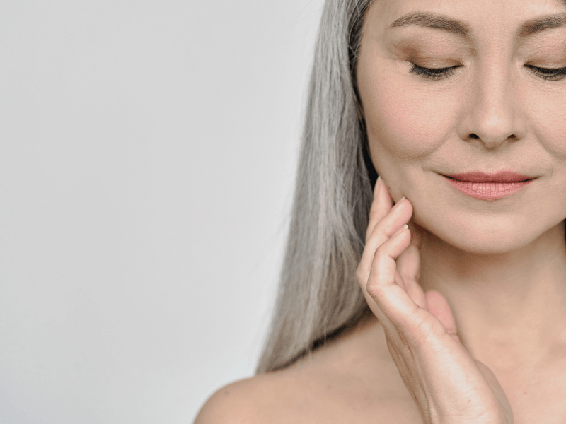 A close up of a woman with gray hair touching her face after Botox.