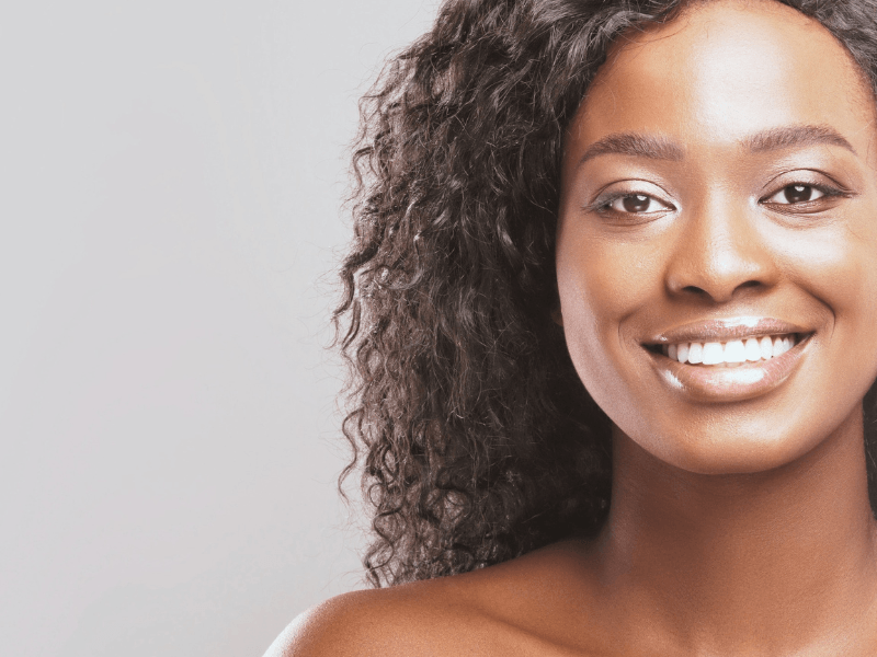 A woman with curly hair is smiling after teeth whitening and looking at the camera.