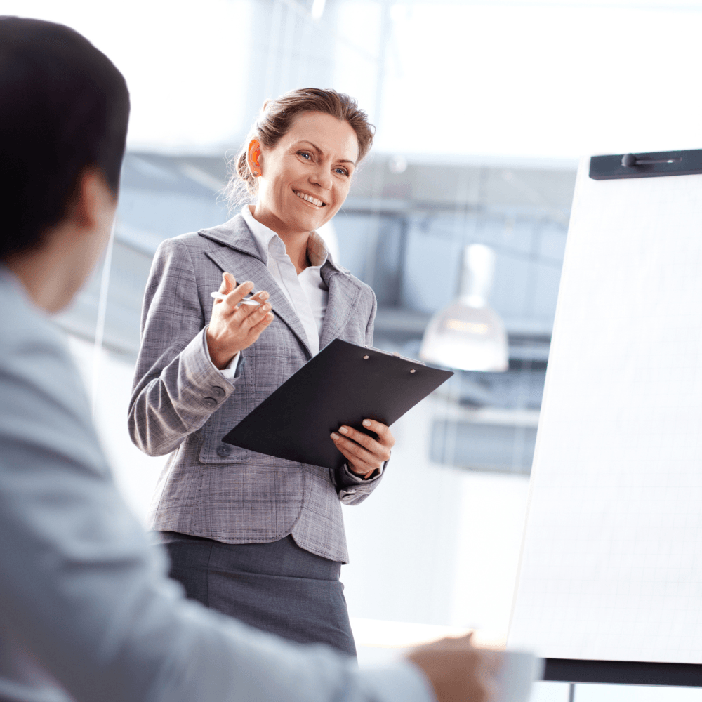 A woman is giving a presentation to a man while holding a clipboard.