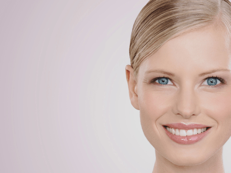 A close up of a woman 's face with blue eyes smiling with her new porcelain veneers.