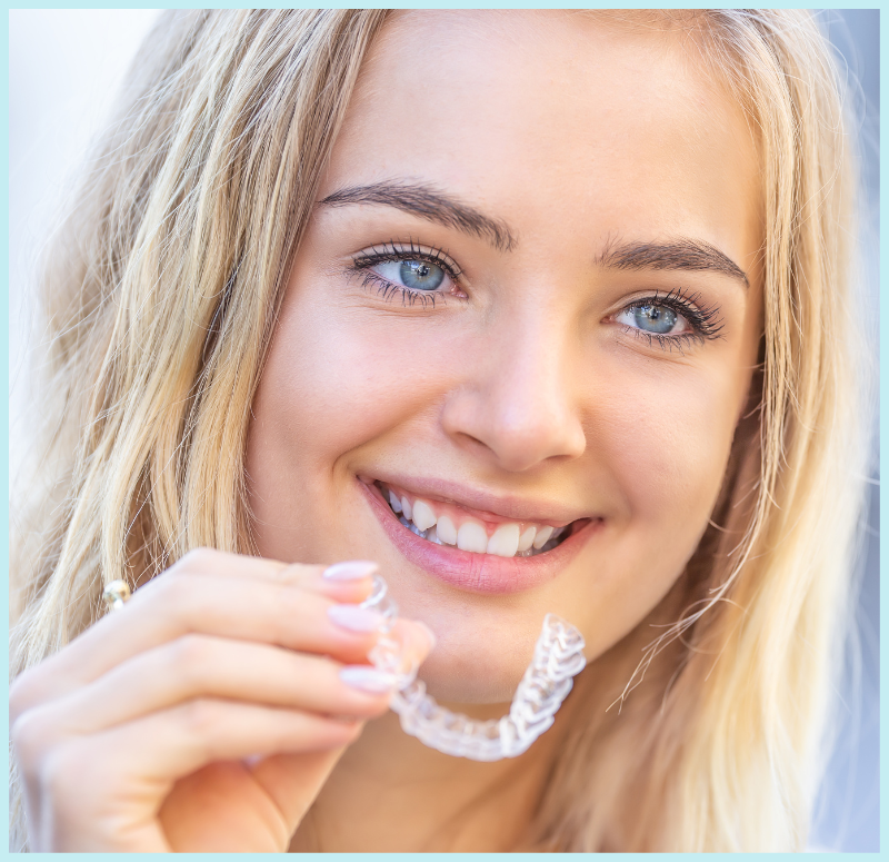 A woman is smiling while holding a clear retainer in her hand.