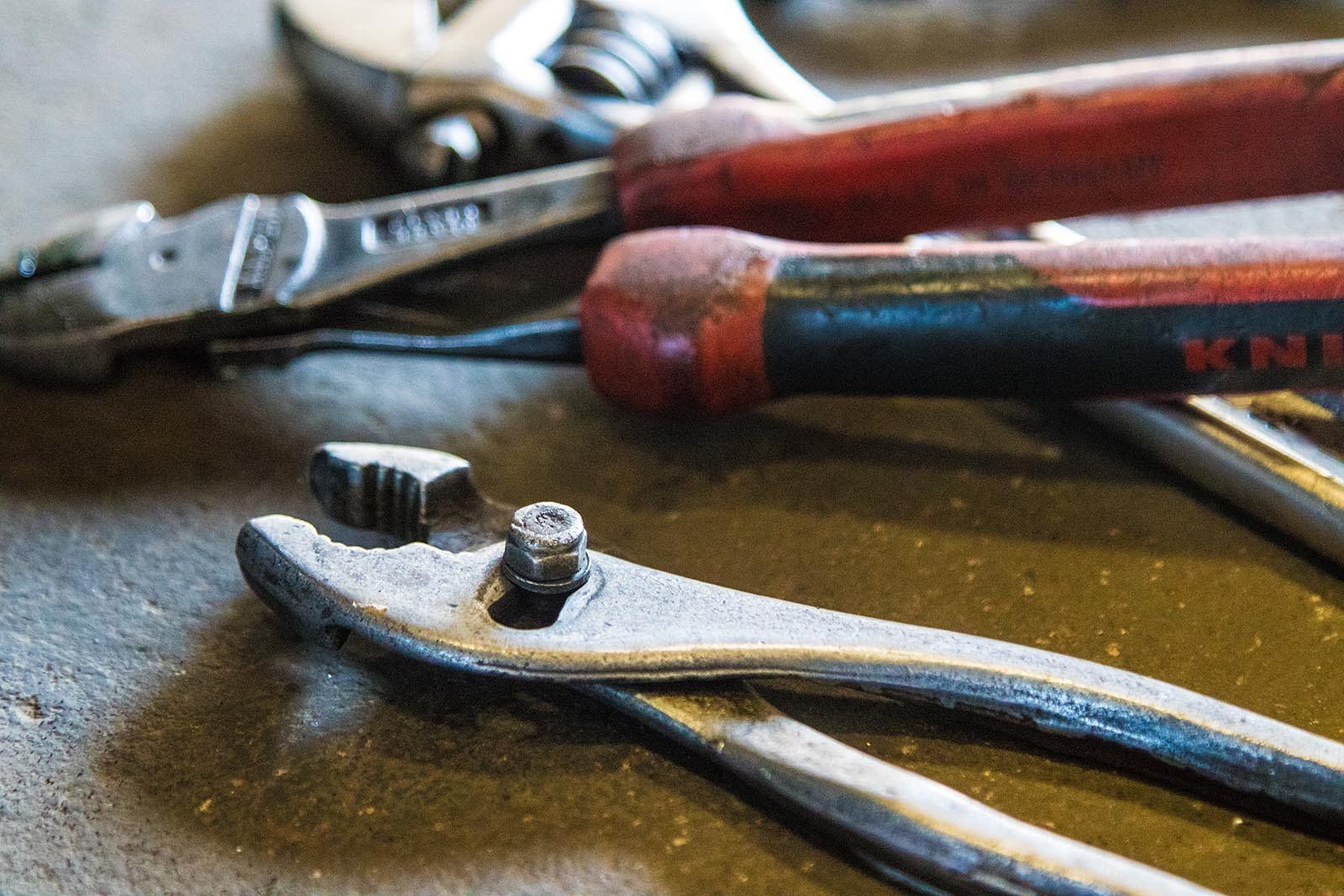 Close-up of worn workshop pliers and hand tools on a workbench, used for mechanical brake repairs.