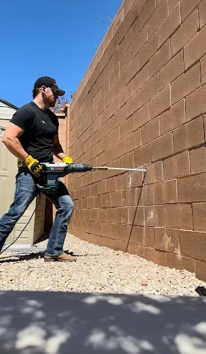 Man using a jackhammer on a brick wall outdoors.