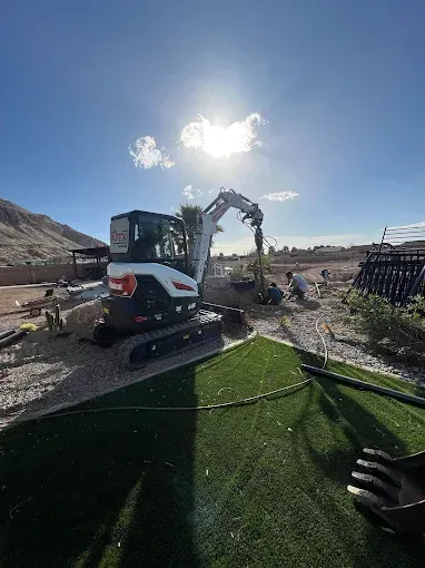 Bobcat excavator on a construction site with sunny sky and artificial grass in foreground.