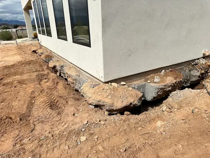 Exterior view of a building corner with a partially installed retaining wall, set in dirt.